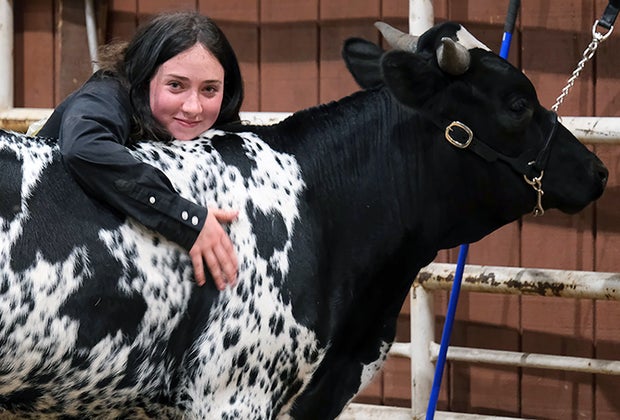Girl in a black shirt hugging a cow for National Day of the Cowboy and Cowgirl