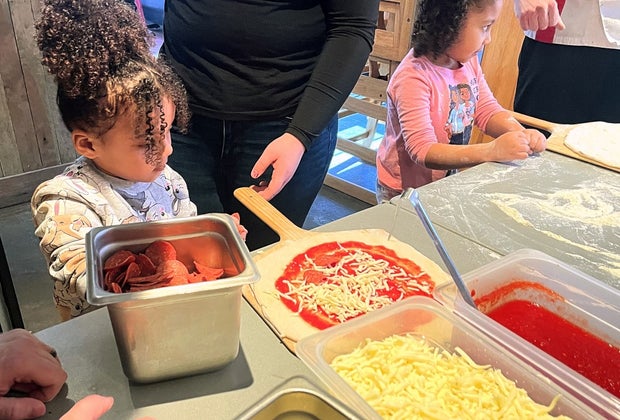 LIttle girl puts cheese on her personal pizza at a Square Peg Pizzeria pizza-making class